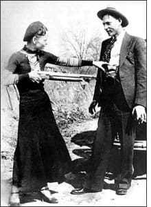 Two people posing with a rifle outdoors.